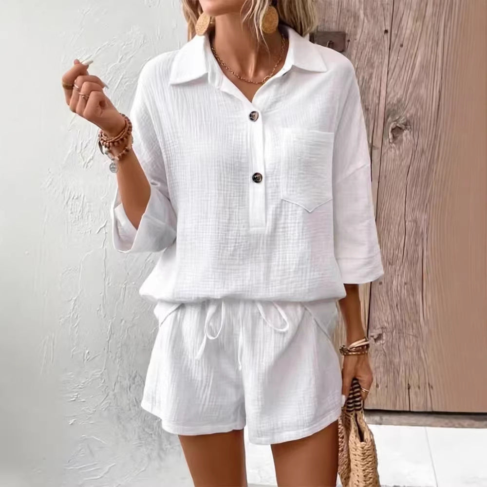 A woman wearing a matching button-down lapel shirt and shorts set in either white or light blue, featuring a soft, textured fabric.