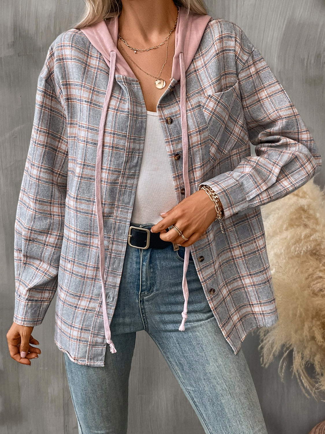 A woman wearing a casual long sleeve plaid jacket with an attached hood, buttoned front, and multiple pockets.
