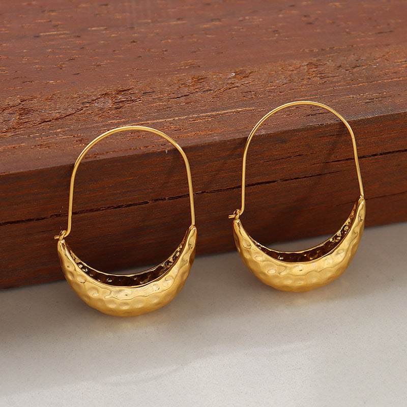 Modern boat-shaped embossed gold drop earrings on a woman