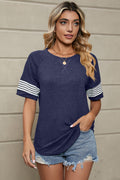 A woman wearing a navy blue short-sleeve t-shirt with white and navy striped detailing on the sleeves.