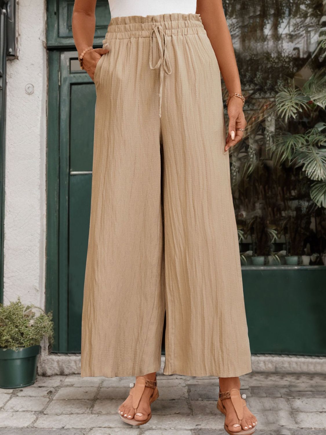 Model wearing beige wide leg pants with a frill tie-waist detail in a casual outdoor setting.