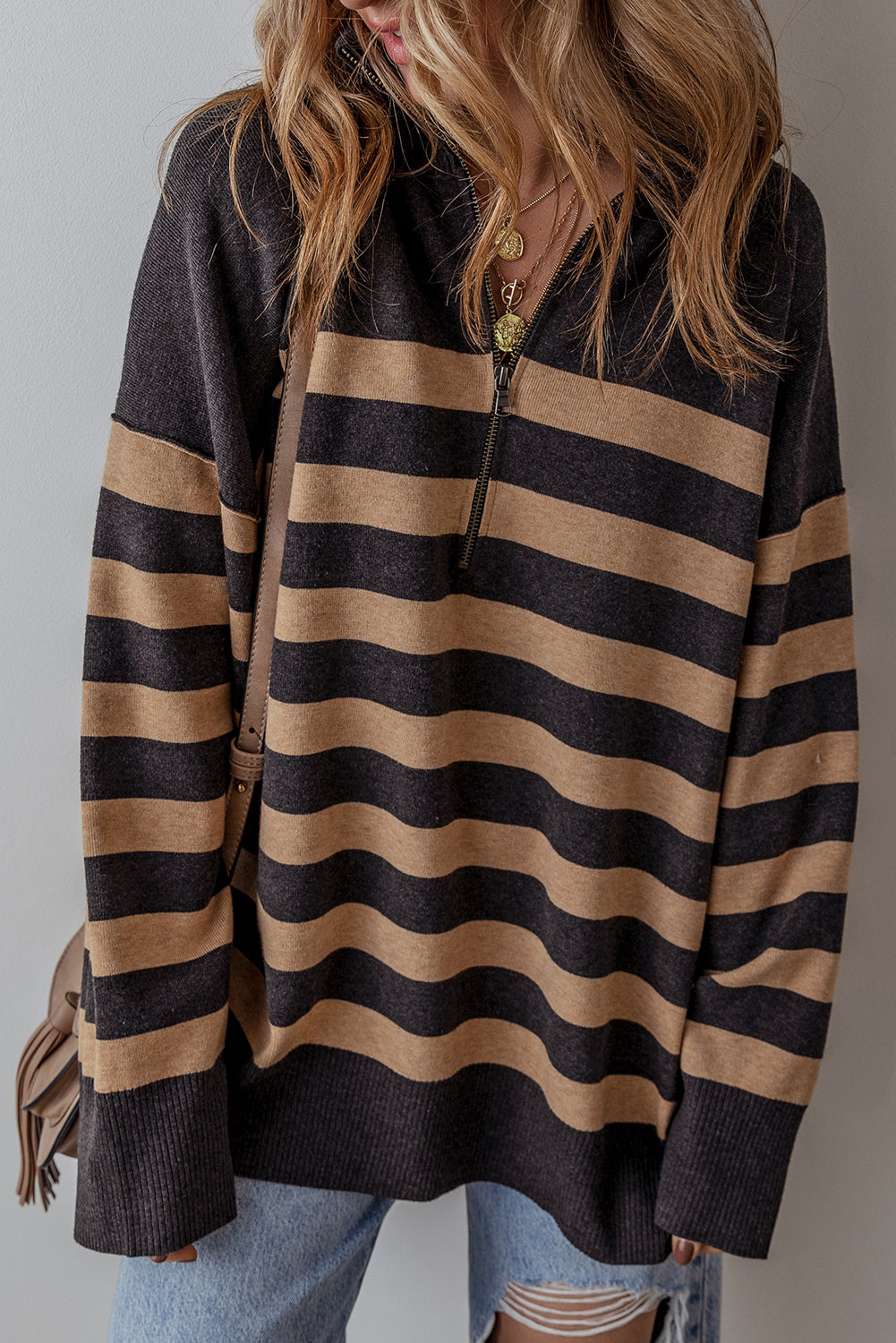 Person wearing a black and beige striped sweater with a plain background