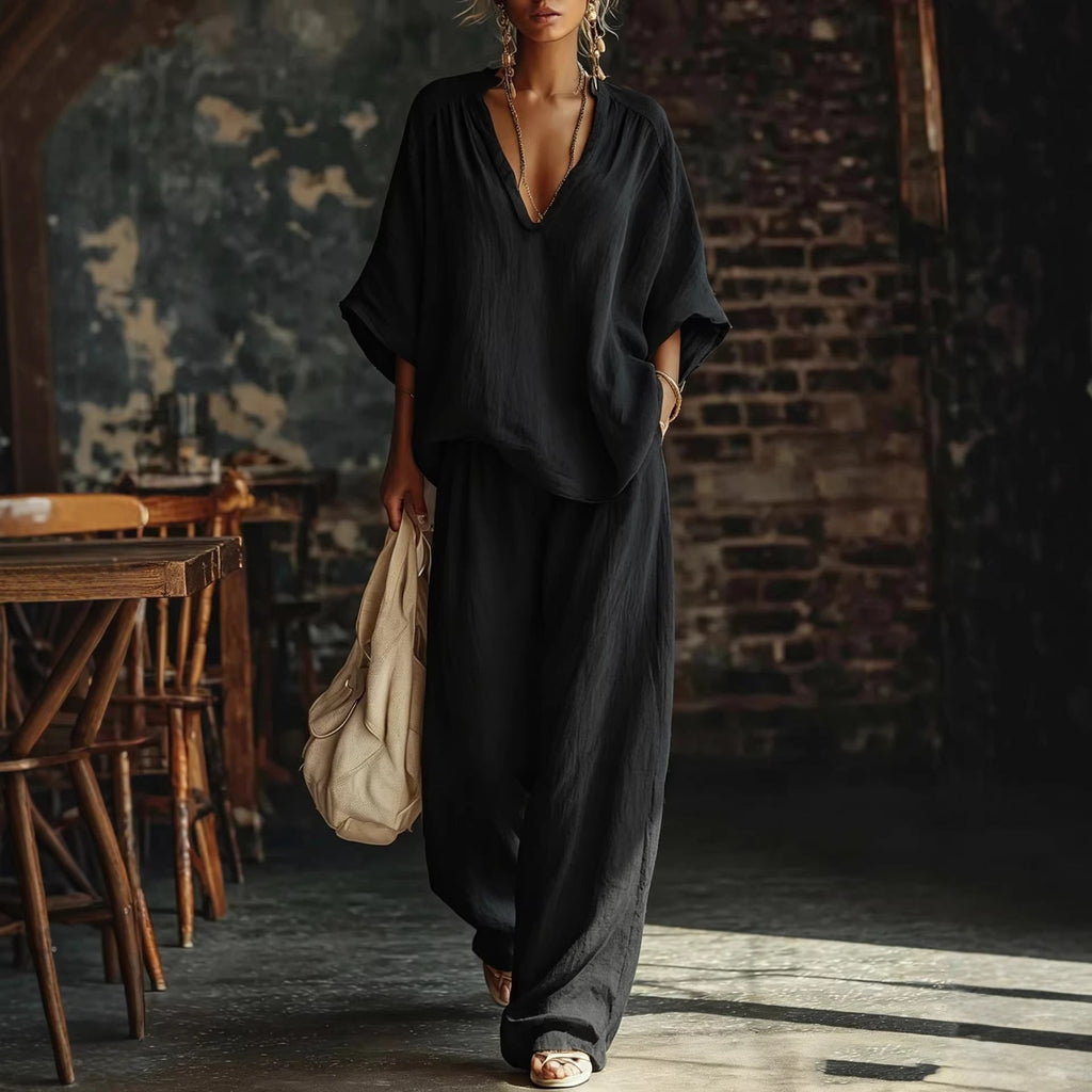 Model wearing a black two-piece loose V-neck short sleeve top and wide leg pants set.