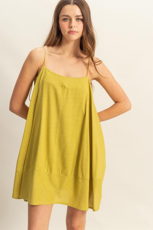 Woman wearing an A-line flowy mini cami dress with side pockets in a summer setting.