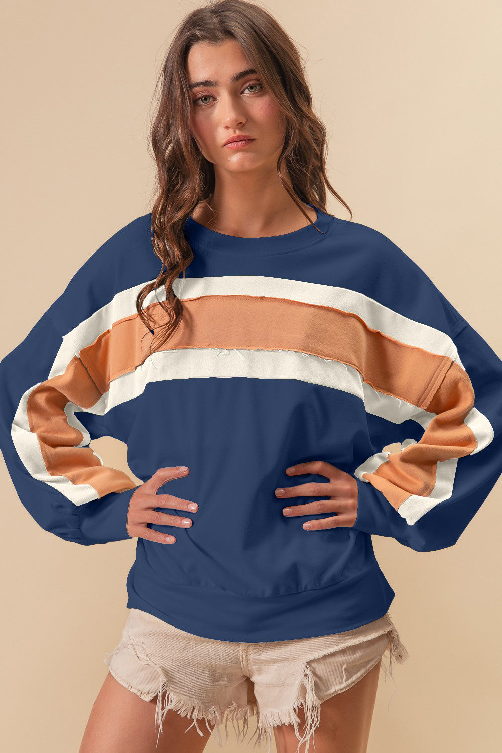 A woman wearing a navy blue, white, and tan color block sweatshirt with raw edge detailing.