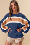 A woman wearing a navy blue, white, and tan color block sweatshirt with raw edge detailing.