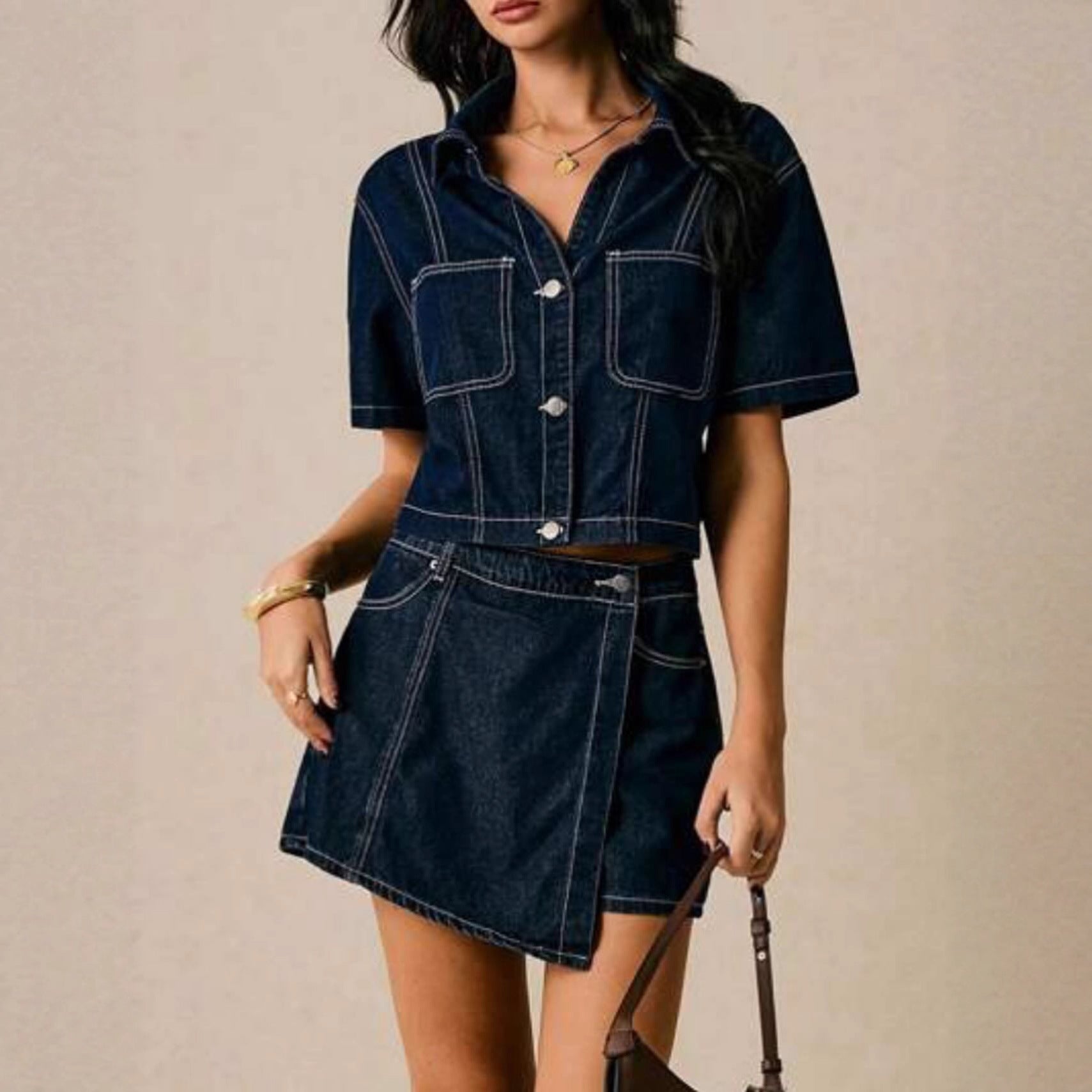 A woman wearing a loose-fit dark blue cotton denim short-sleeve shirt-dress with matching pants and contrast white stitching.