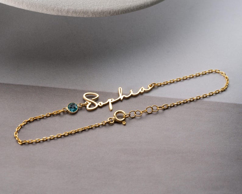 Personalized cursive name bracelet with a round bezel-set birthstone on a delicate cable chain