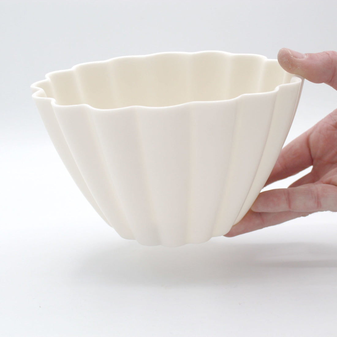 A cream-colored, fluted porcelain candle holder being held, showcasing its textured design and translucent quality when lit.