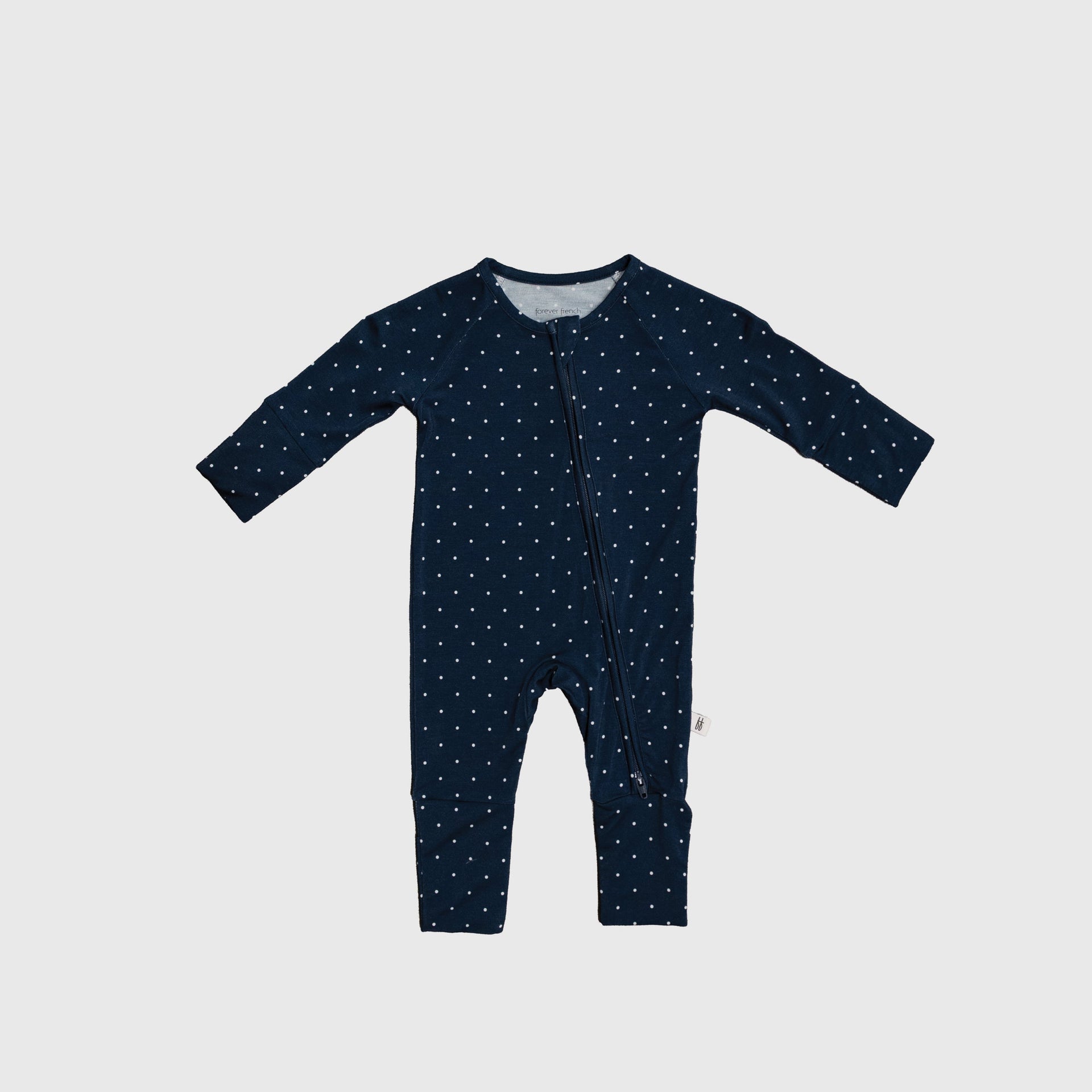 Baby wearing modern navy and white polka dot bamboo zip pajamas with convertible cuffs.
