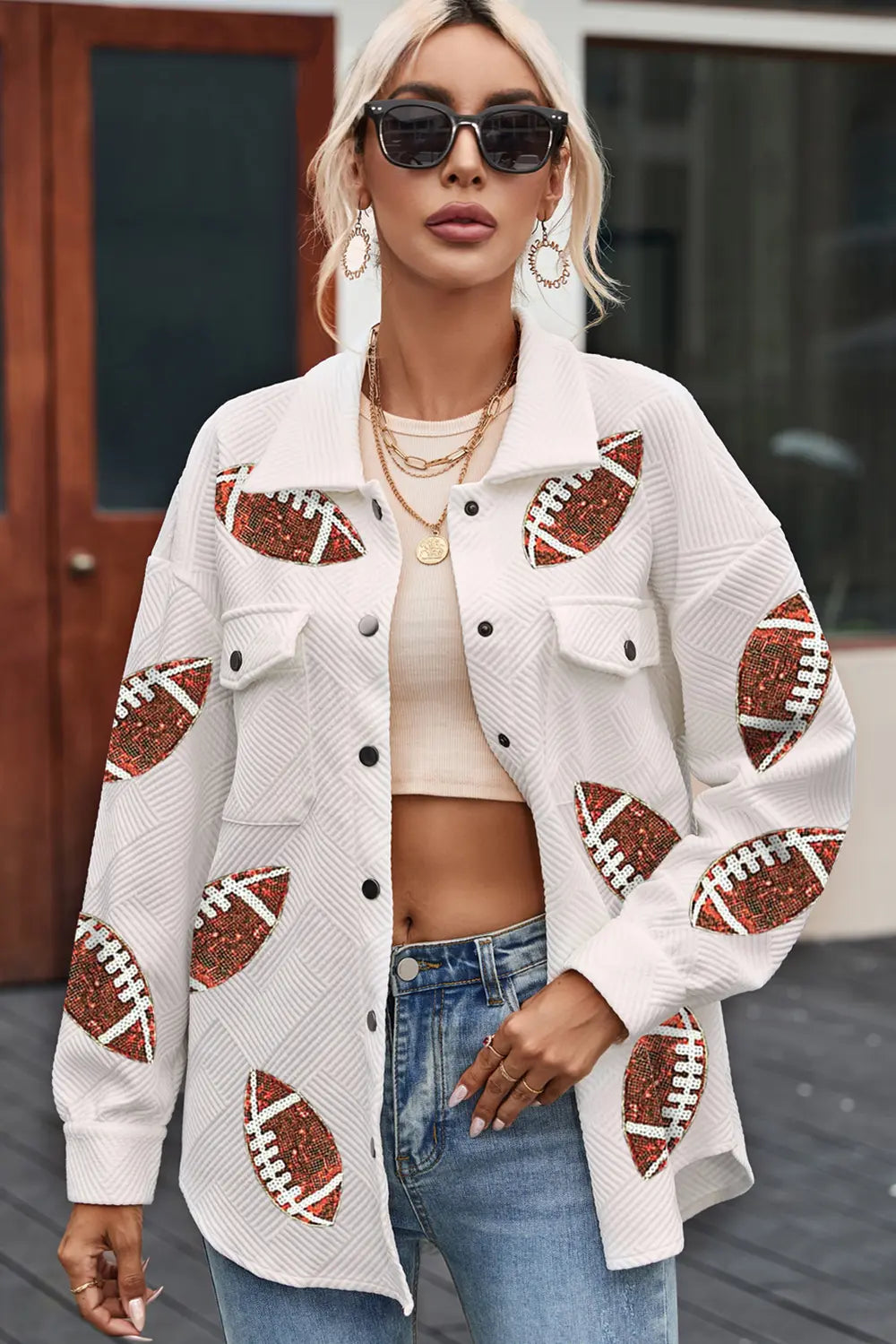 A woman wearing a white collared jacket with sequin football patches, buttoned down with snap closures.