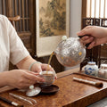 Handcrafted 999 fine silver teapot decorated with chased peony blossoms, an ebony handle, and a pale jade lid finial.