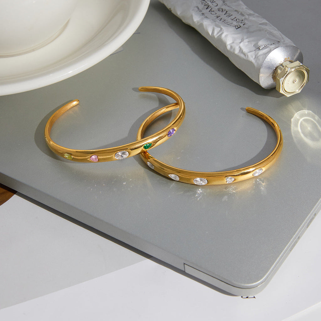 Elegant gold open bangle set with colorful zircons on a white minimalist background.