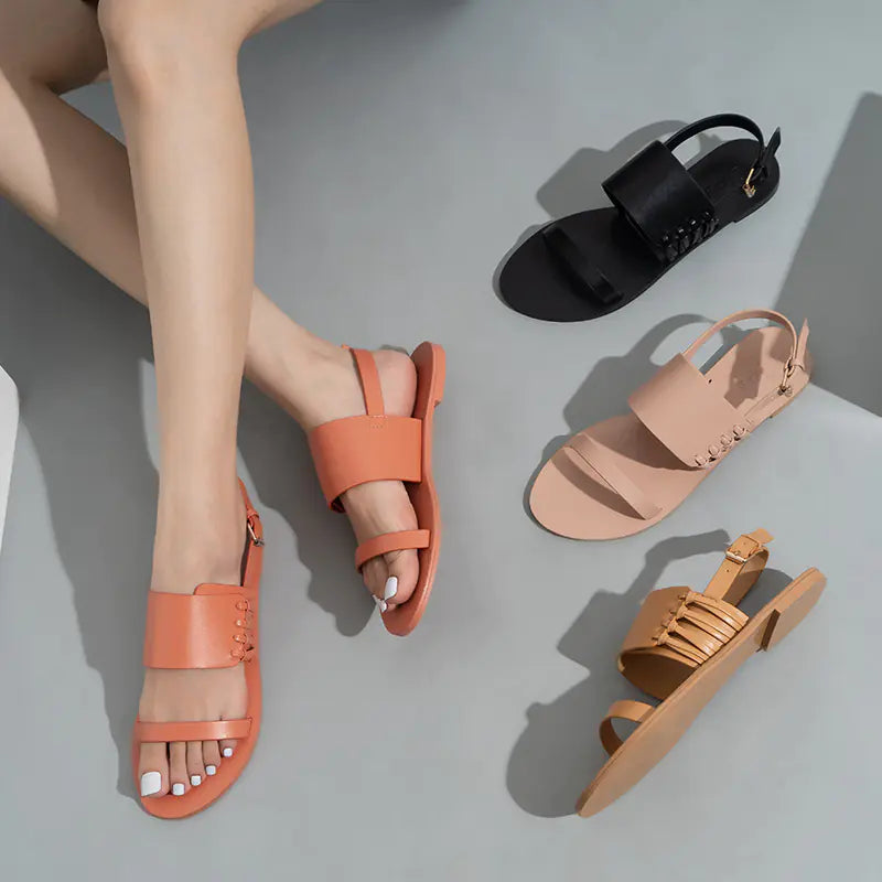 Top-down view of multiple pairs of flat strappy summer sandals in black, peach, and tan colors on a neutral background.