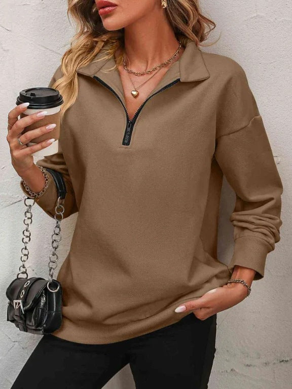 Woman wearing a brown long-sleeve top with a zipper, holding a coffee cup and a black handbag.