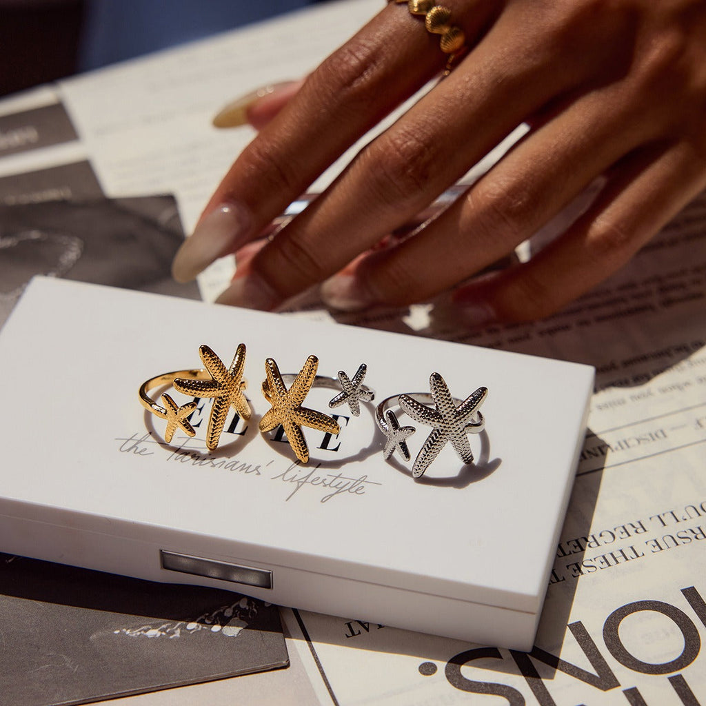 Close-up of a gold starfish and shell-themed adjustable titanium steel ring on a woman's hand.
