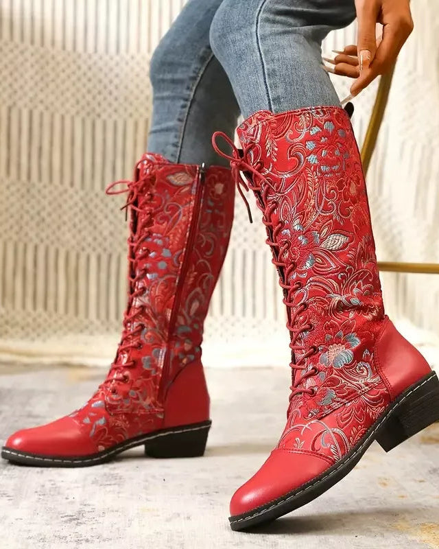 Red embroidered knee-high boots worn with blue jeans on a neutral background