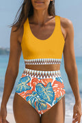 Model wearing a yellow high-waisted bikini set with geometric contrast trim and tropical leaf print pattern on the beach.