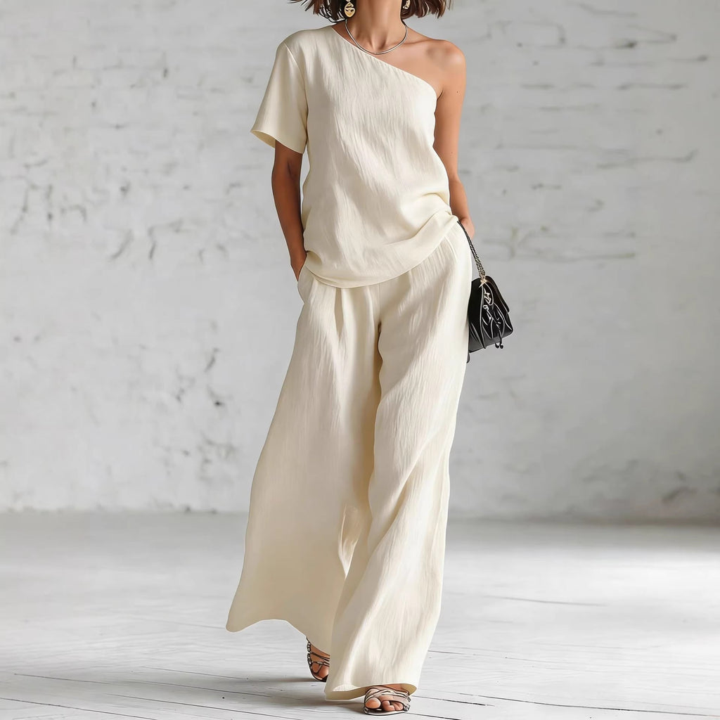 A woman wearing a stylish matching two-piece set featuring a one-shoulder top and wide-leg trousers.