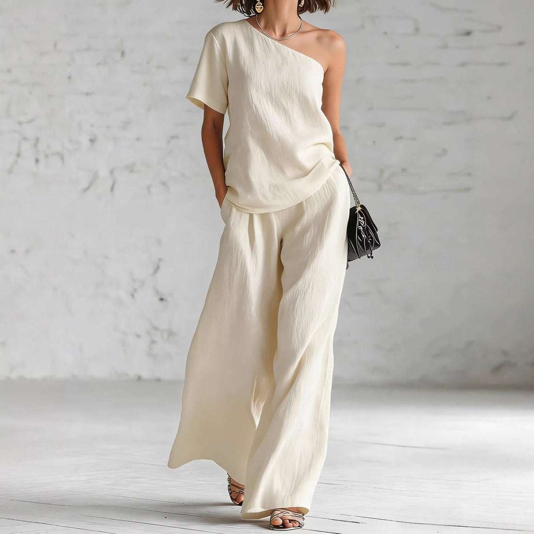 A woman wearing a stylish matching two-piece set featuring a one-shoulder top and wide-leg trousers.