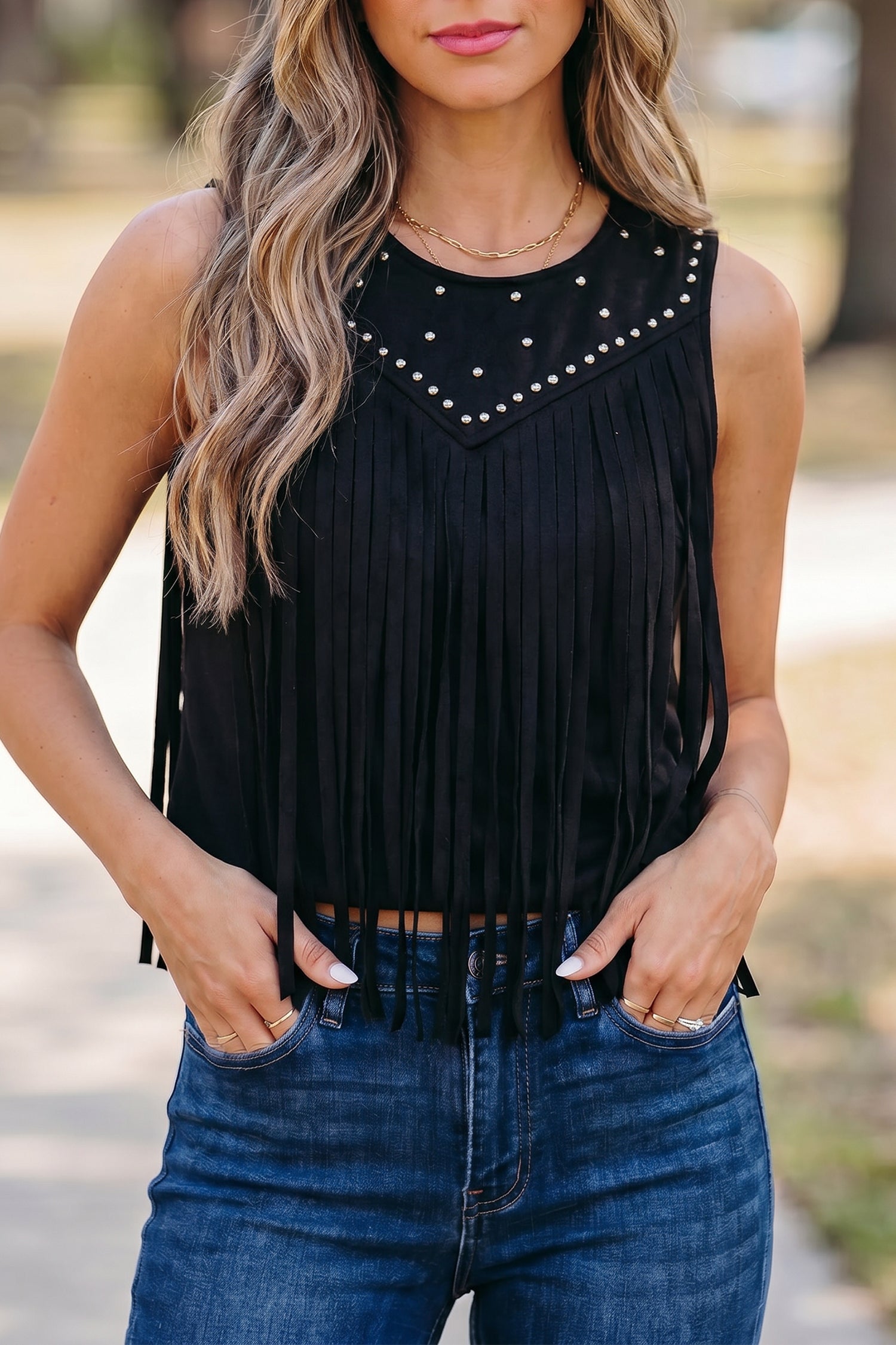 Black sleeveless top with rivet-accented bust paneling and fringe detailing, styled for a western-inspired bohemian look.