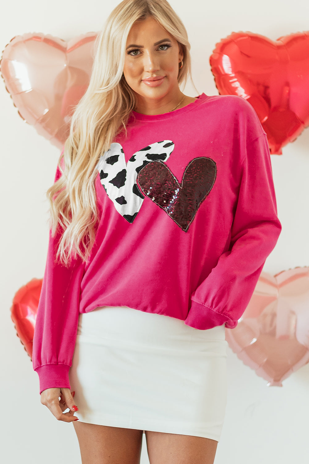 A woman wearing a vibrant hot pink sweatshirt with a cow print and sequin double heart patch on the front