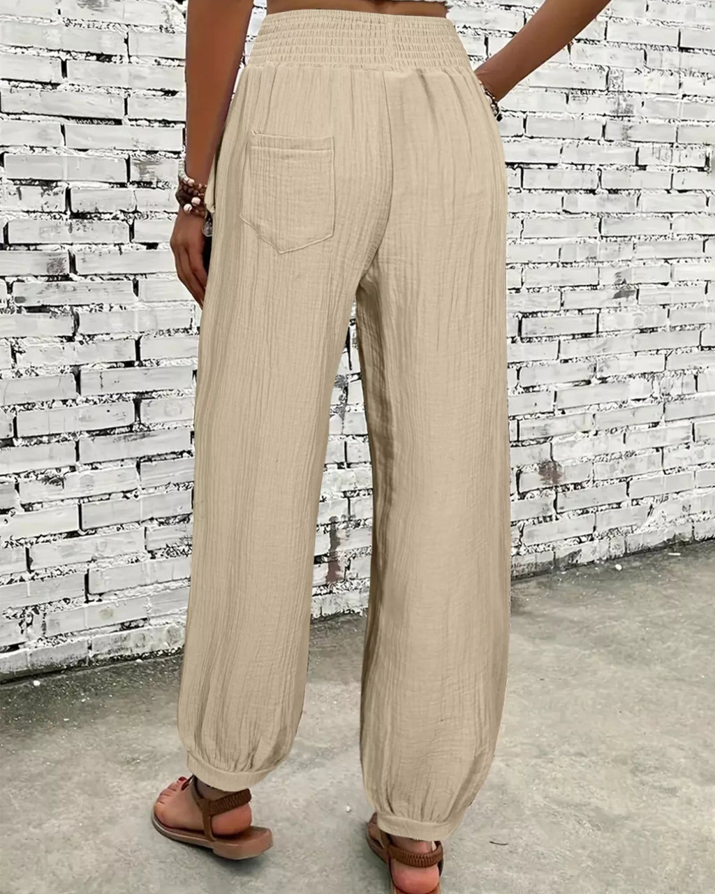 Person wearing beige wide-leg pants against a textured white brick wall.