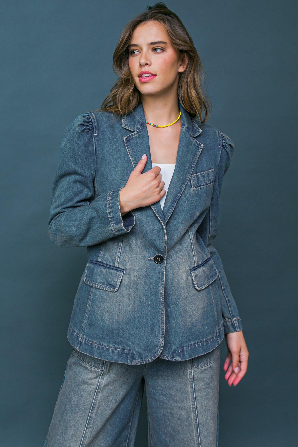 A woman wearing a washed denim blazer with puff shoulders and a single button closure.