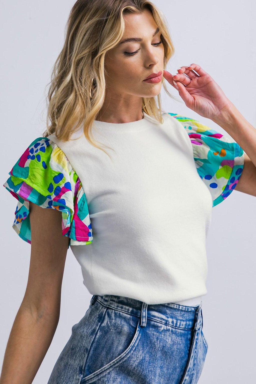 A woman wearing a white short-sleeve knit sweater with colorful abstract print double ruffle sleeves and a ribbed hem.