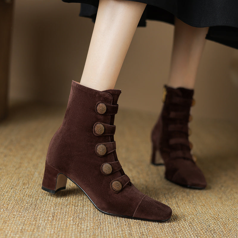Close-up of a pair of brown suede ankle boots on a model, featuring a block heel and decorative button detailing.