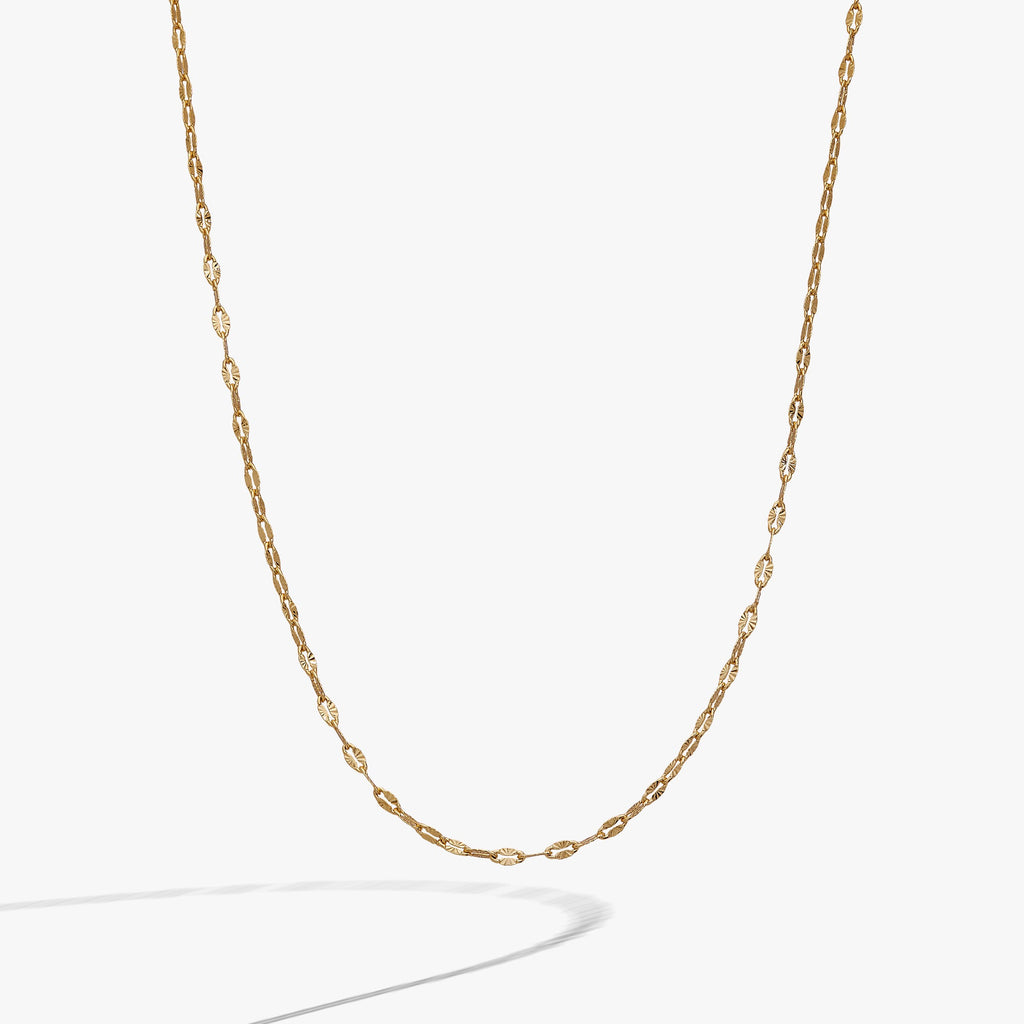 Gold multi faceted lip chain necklace resting on a neutral background, highlighting the light-catching texture.