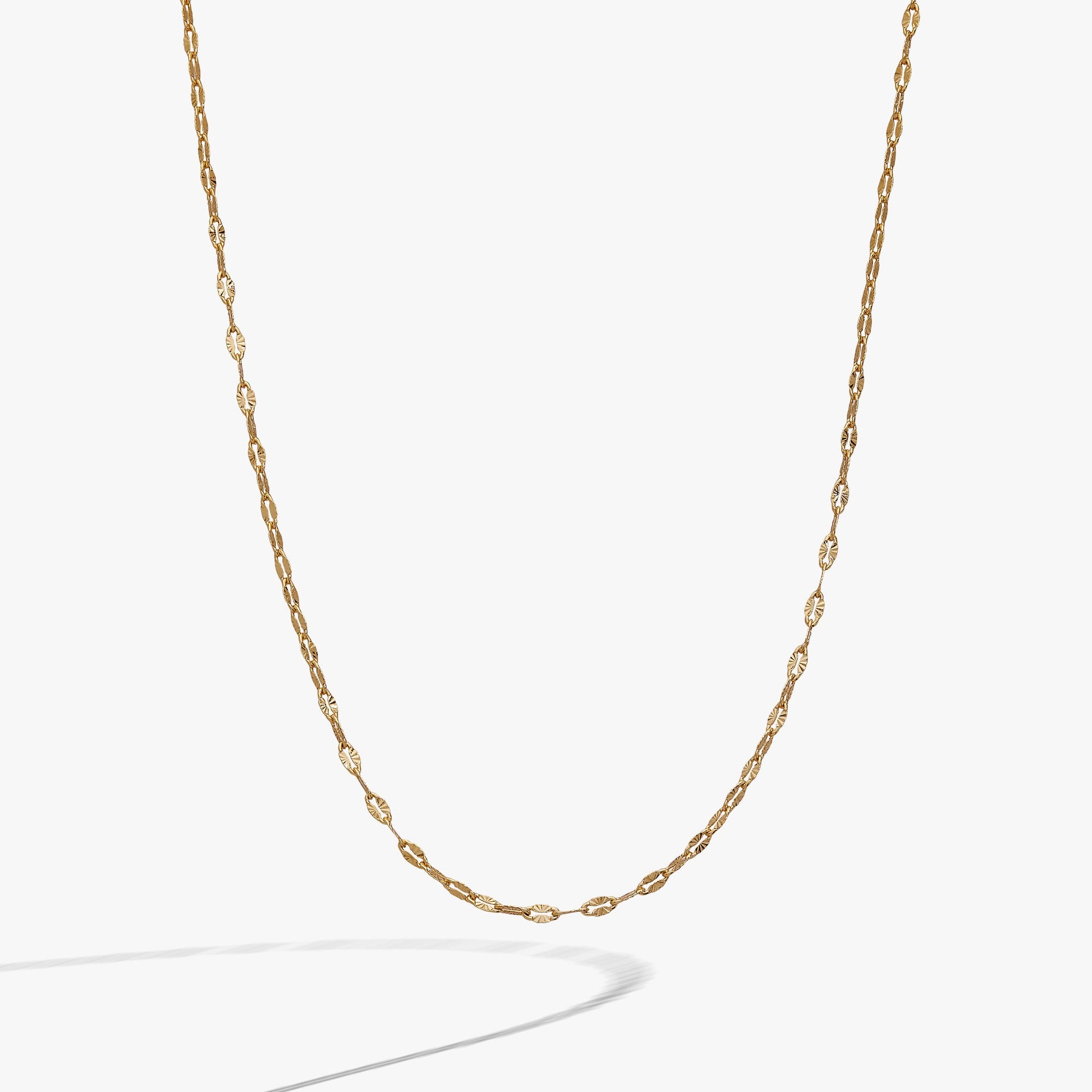 Gold multi faceted lip chain necklace resting on a neutral background, highlighting the light-catching texture.