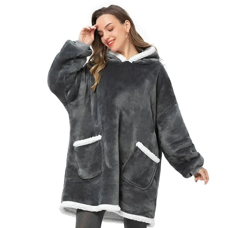 Person wearing an oversized soft flannel blanket hoodie with sleeves and hood in a cozy home setting
