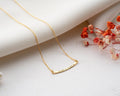 Minimalist curved bar necklace customized with a name, displayed against a neutral background.
