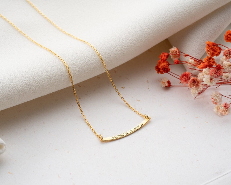 Minimalist curved bar necklace customized with a name, displayed against a neutral background.