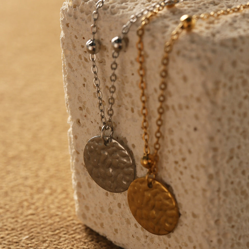 Close-up of a Vera Lux 18K gold-finished round disc pendant with embossed texture on a delicate chain