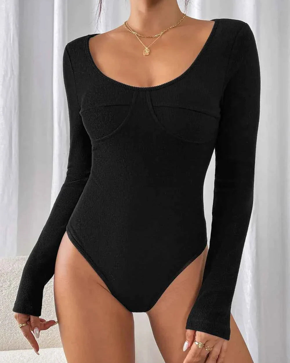 Black bodysuit with long sleeves worn by a model against a neutral background