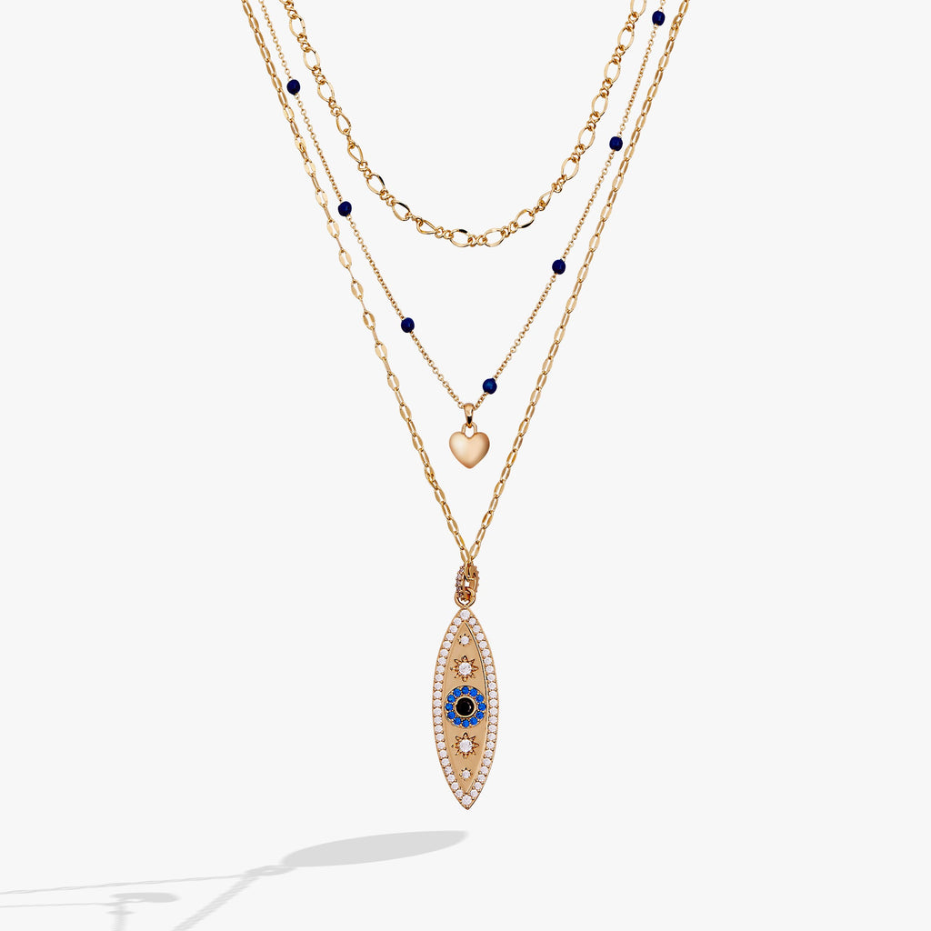 Three-strand gold layered necklace featuring a blue evil eye pendant, a puffy heart, and crystal accents.