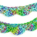 Close up of a vibrant, multi-colored crocheted scallop garland hanging in a bohemian living room setting.