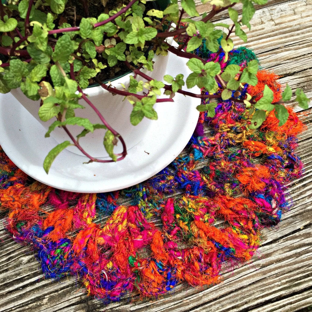 A vibrant, kaleidoscopic crochet doily in orange, purple, blue, green, and yellow on a wooden table.