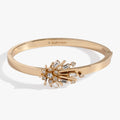 Gold-tone hinge bangle featuring a starburst emblem decorated with sparkling clear crystals.