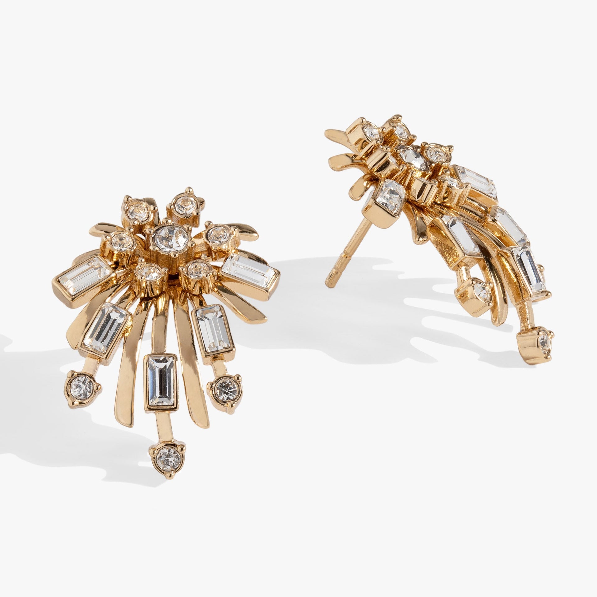 Gold-tone starburst stud earrings featuring clear crystals on a white background.