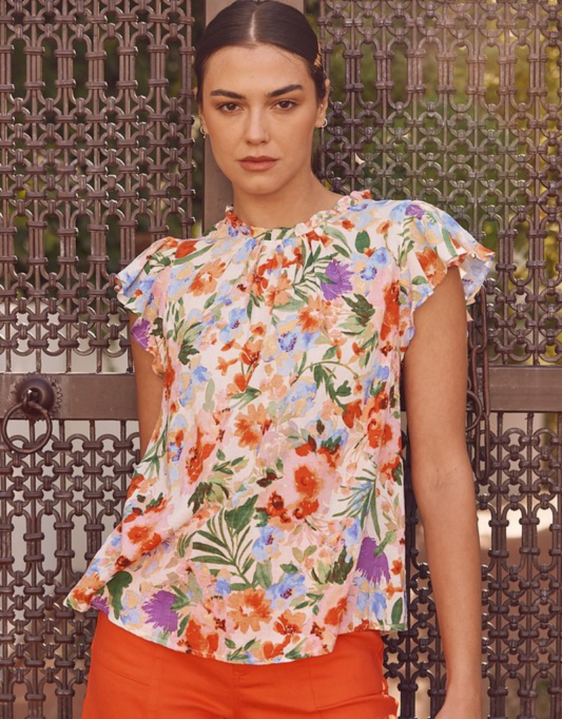 A woman wearing a red flutter sleeve blouse with floral print and ruffled shoulder detail, viewed from the front.