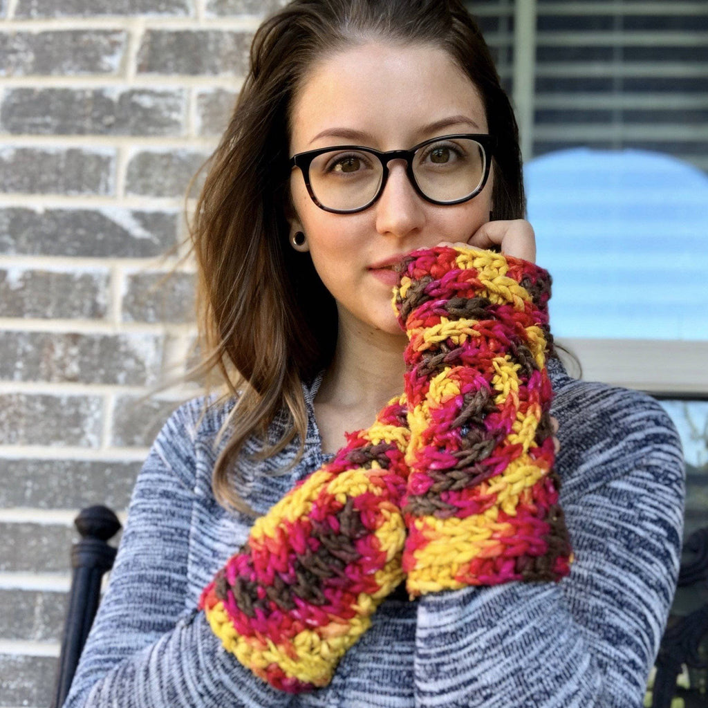 Close up of bohemian freeform crochet fingerless mittens in yellow, magenta, and brown yarn with a spiral pattern.