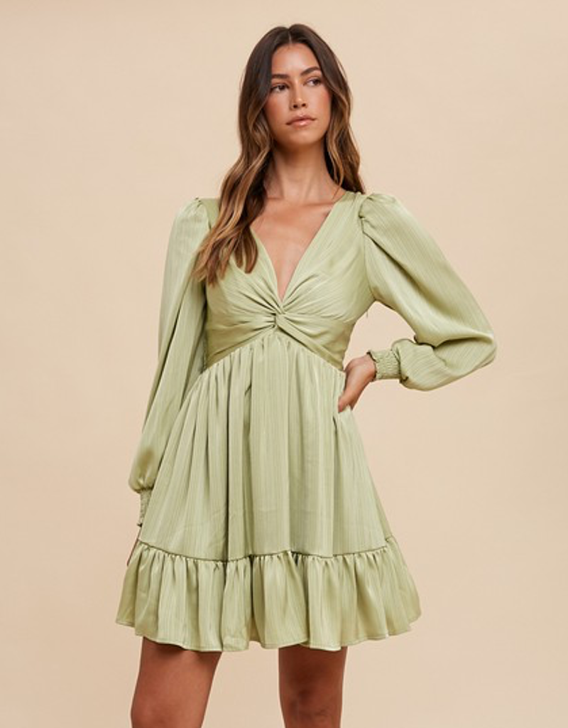 A woman wearing a long-sleeve front twisted satin mini dress in a soft pistachio green color, styled for a party.