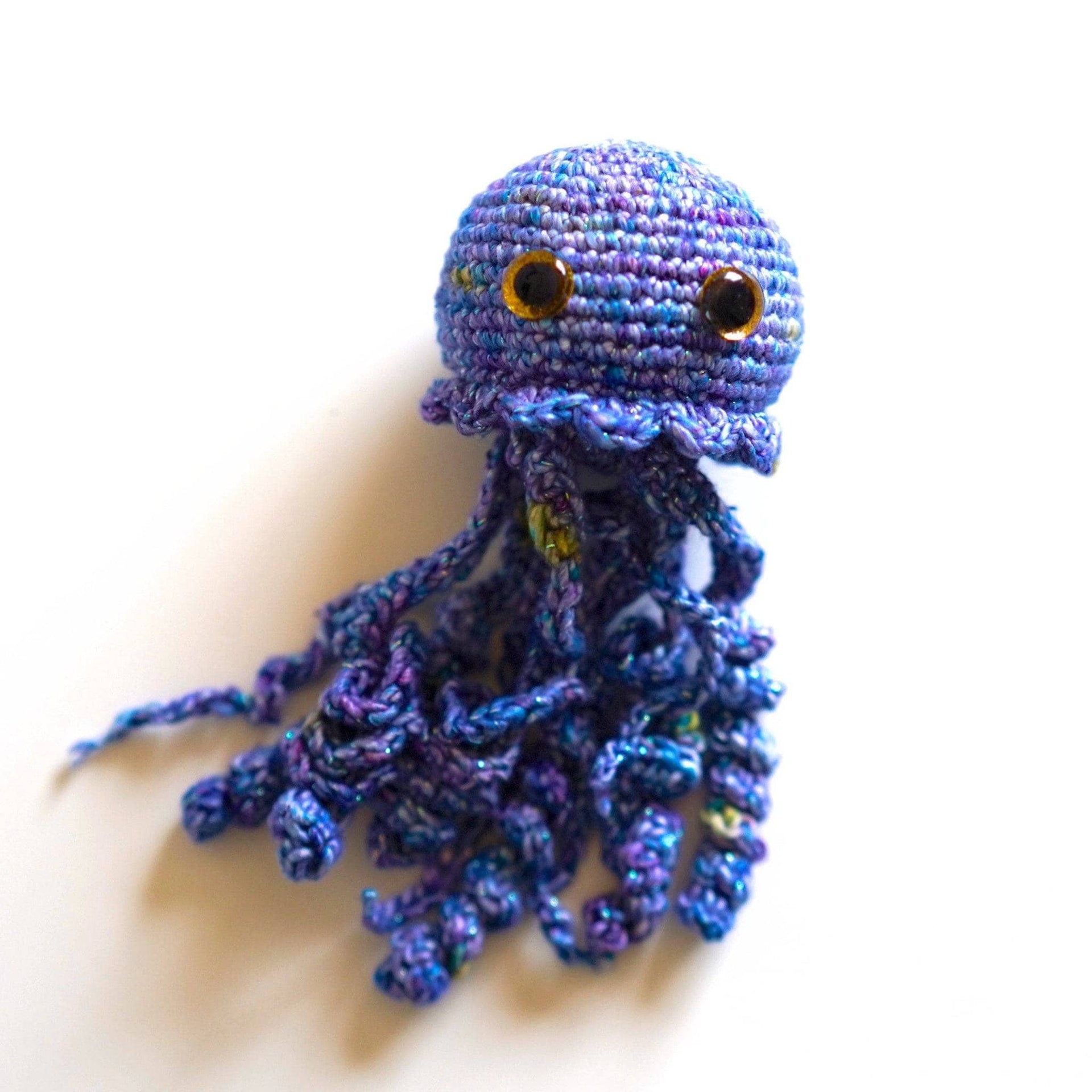 Finished Galaxy Jellyfish amigurumi in shades of blue and purple sitting on a wooden table.