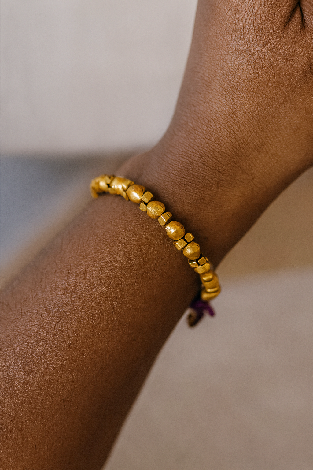 Close-up of a bohemian-style Nefassilk bracelet with hammered brass beads and a purple string accent on a wrist.