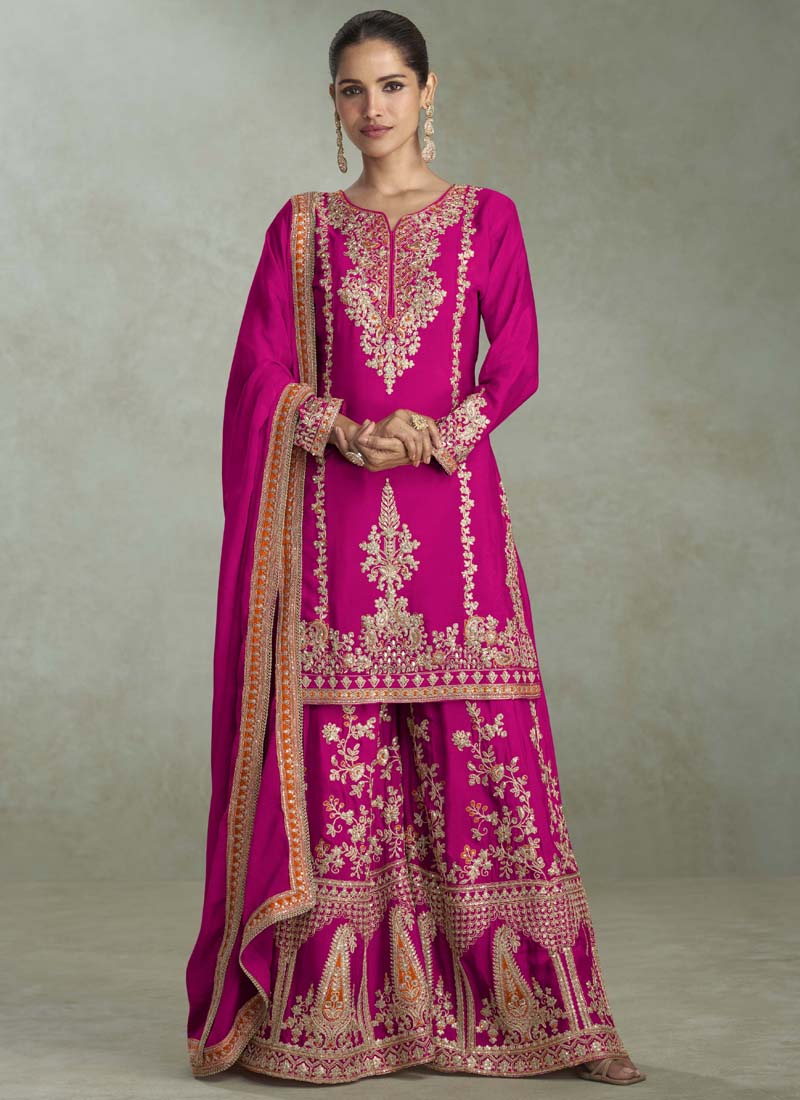 A woman wearing a rani pink chinon designer palazzo suit with intricate gota patti embroidery.