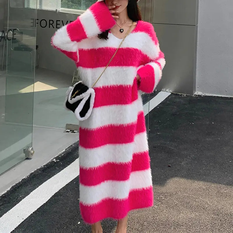 A woman wearing a long, fuzzy striped knitted pullover dress in pink and white, paired with a shoulder bag.