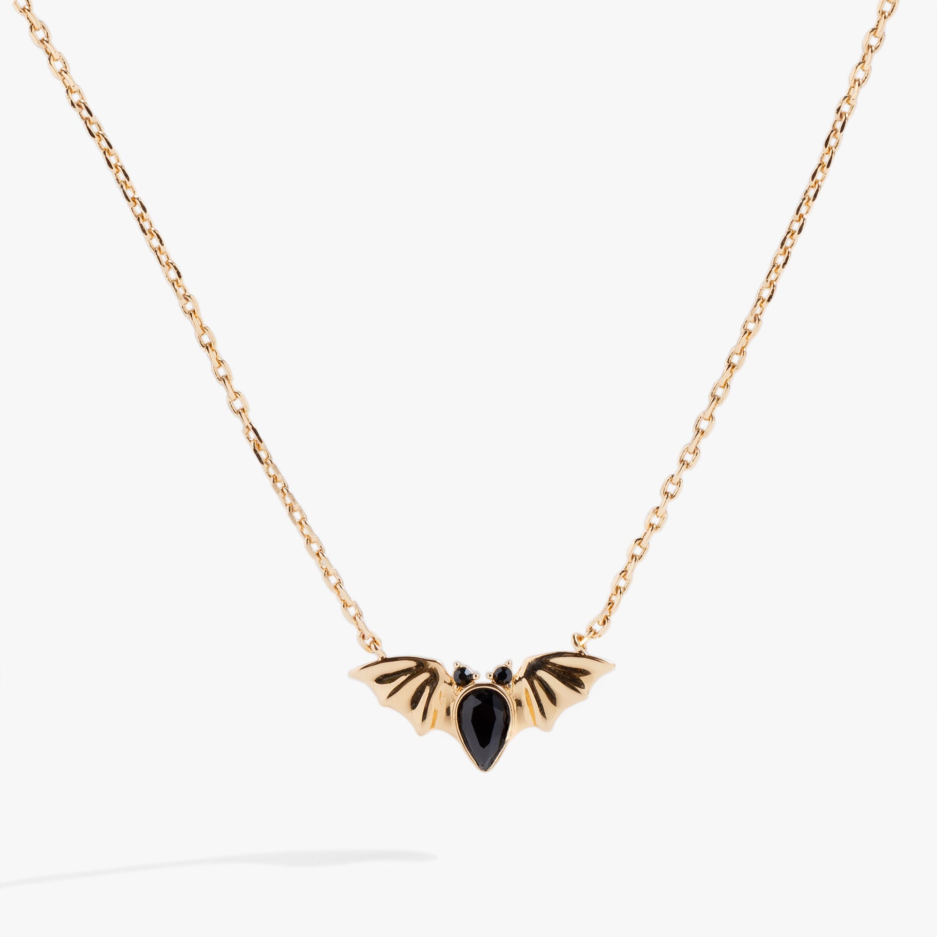 Close up of a silver bat-shaped pendant featuring three black pear-cut crystals on a silver cable chain.